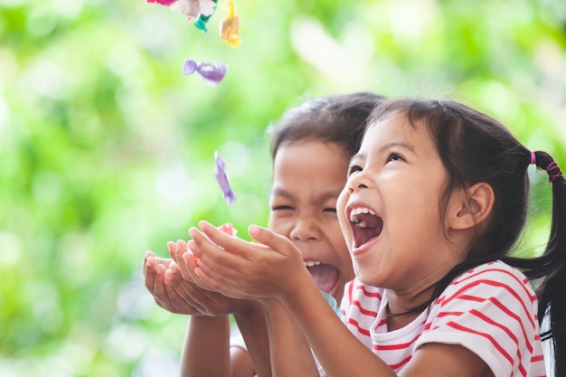 Zwei asiatische Kindermädchen, die Spaß haben, die Süßigkeiten zu fangen, die vom Himmel fallen