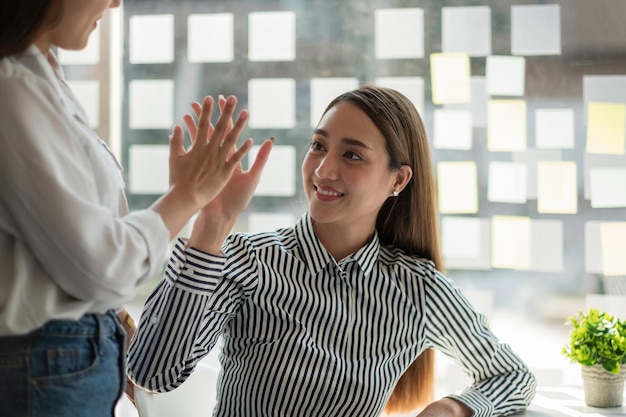 Zwei asiatische Kolleginnen geben sich gegenseitig High Five Erfolgreiches Konzept für die Zusammenarbeit von Geschäftsteams