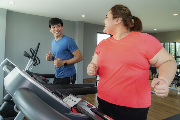 Zwei asiatische Trainer Mann und übergewichtige Frau, die Training auf Laufband im Fitnessstudio, Trainer Schlag auf