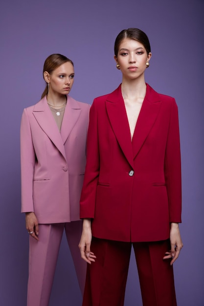 Zwei asiatische und europäische Modemodelle in zartrosa und rot übergroßen Anzügen, Jackenhosen