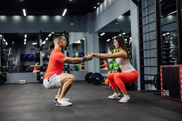 Zwei Athleten, eine schöne Frau und ein gutaussehender Mann, hocken im Fitnessstudio oder Fitnesscenter