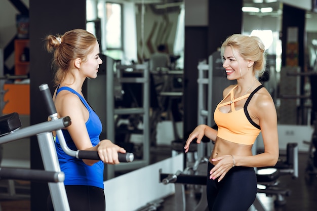 Zwei athletische blonde Frauen, die im Fitnessstudio sprechen, kommunizieren mit Trainer