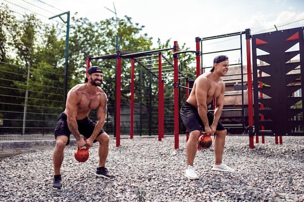 Zwei athletische Männer, die mit einer Kettlebell am Straßenturnhallenyard ausarbeiten.