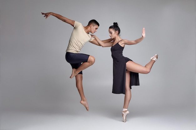 Zwei athletische moderne Balletttänzer posieren vor einem grauen Studiohintergrund.