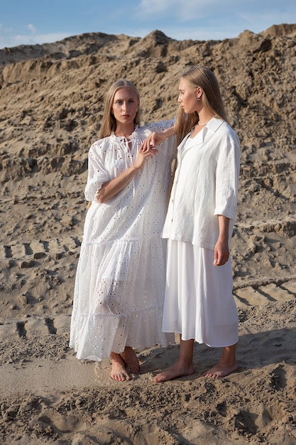 Zwei attraktive junge Zwillingsschwestern, die im Sandsteinbruch in eleganter weißer Kleidung aufwerfen
