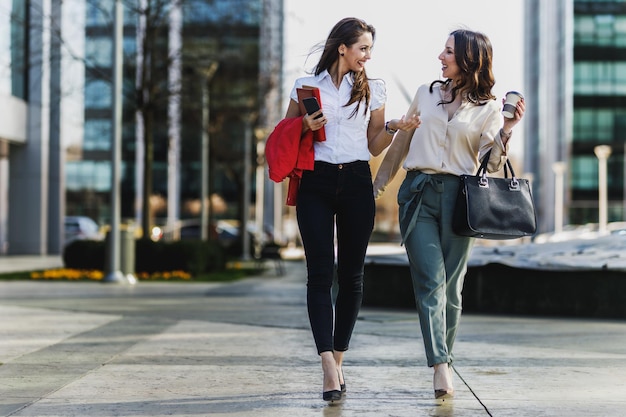 Zwei attraktive lächelnde Geschäftsfrauen unterhalten sich beim Gehen auf dem Weg zur Arbeit.