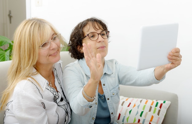 Zwei attraktive reife Frauen, die mit Tablette websurfing sind