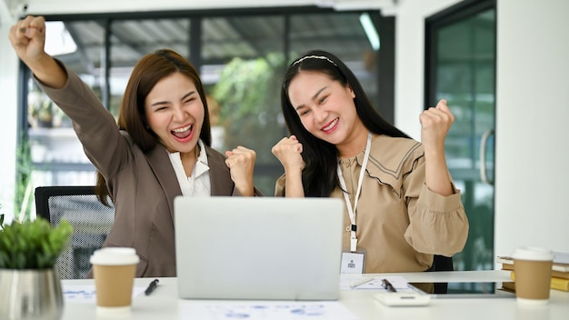 Zwei aufgeregte und überglückliche junge asiatische Geschäftsfrauen schreien vor Freude und jubeln