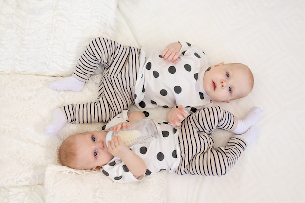 zwei Baby Zwillinge Bruder und Schwester liegen auf dem Bett im Schlafanzug und trinken Milch aus einer Flasche, Babynahrungskonzept, Draufsicht