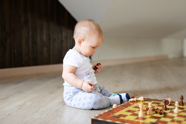 Zwei Babys Junge und Mädchen, die zu Hause Schach auf dem weißen Bretterboden spielen.