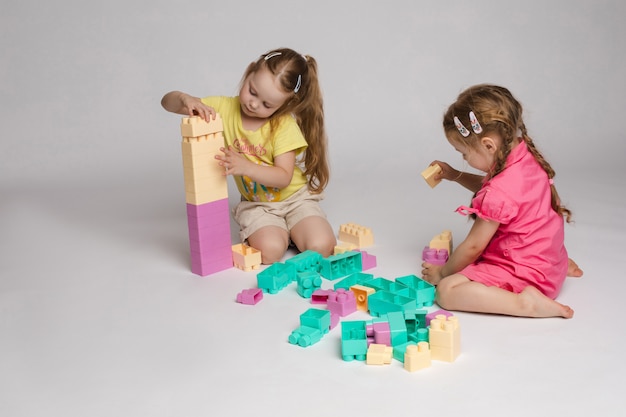 Zwei begeisterte kleine Mädchen spielen zusammenbauen Konstruktor voll Schuss auf Studio weißen Hintergrund