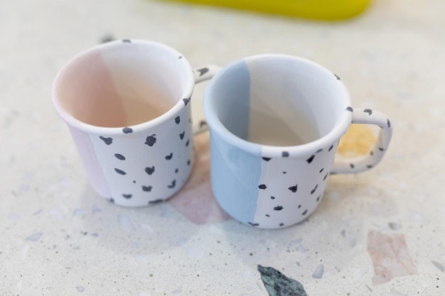 Foto zwei bemalte keramikbecher stehen in einer kunstwerkstatt zum brennen bereit. einfaches muster an einer keramischen teetasse. das ergebnis der arbeit des studenten während der meisterklasse. geringe schärfentiefe