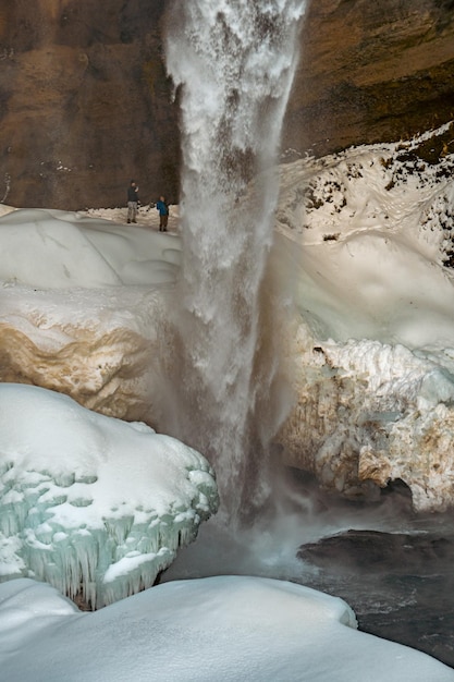 Zwei Bergtouristen hinter dem gefrorenen Kvernufoss-Wasserfall mit Schnee und Stalagmiten