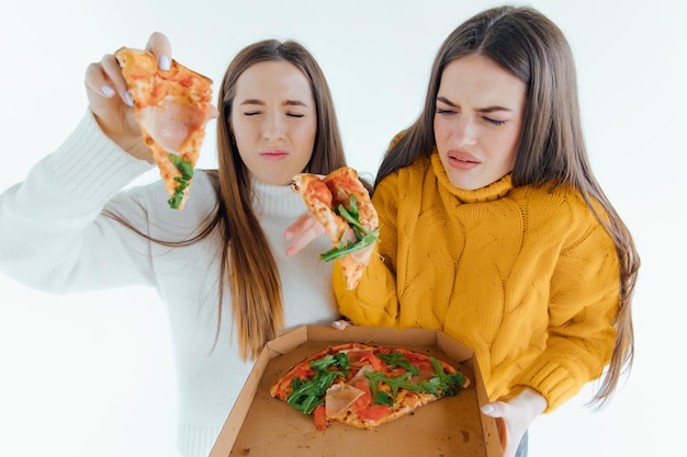 Zwei beste Freunde, die appetitanregende Pizza essen. Mädchen lächeln, blicken in die Kamera und posieren.