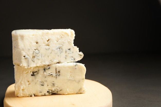 Zwei Blauschimmelkäse im Stapel auf Holzbrett. Dreieckiges Stück Gorgonzola-Käse.