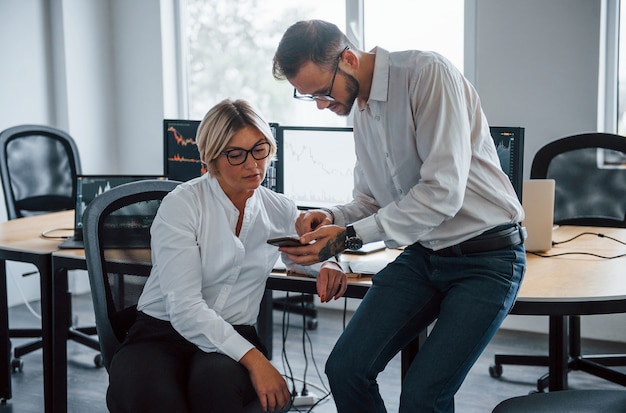 Zwei Börsenmakler in formeller Kleidung arbeiten im Büro mit Finanzmarkt.