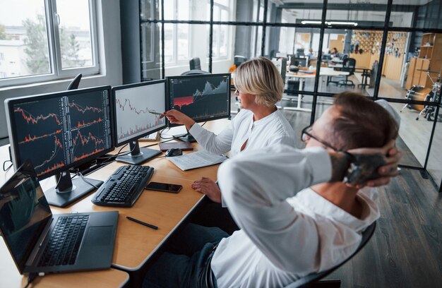 Zwei Börsenmakler in formeller Kleidung arbeiten im Büro mit Finanzmarkt.