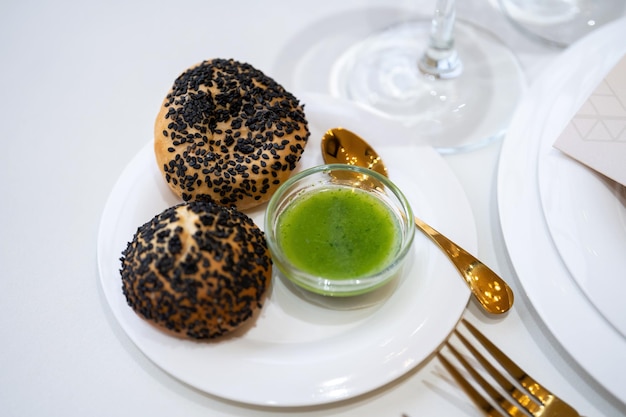 Zwei Brötchen mit schwarzem Sesam auf einem schönen Tisch mit weißer Tischsoße und vergoldeten Gerichten