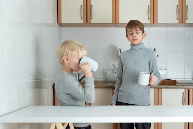 Zwei Bruderjungen stehen in der Küche mit Tassen in ihren Händen Familienfrühstück