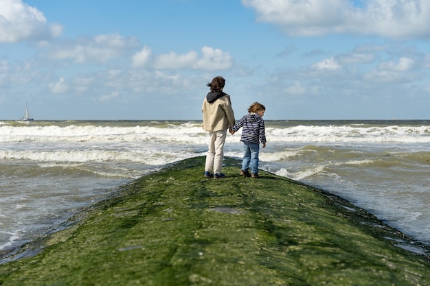 Zwei Brüder halten sich Händchen haltend auf einem Wellenbrecher an der Nordsee. Jungen verbringen Wochenende am Meer in Belgien, Knokke. Geschwisterfreundschaft.