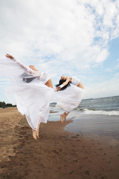 Zwei charmante Mädchen im weißen Kleid, die an der Küste springen