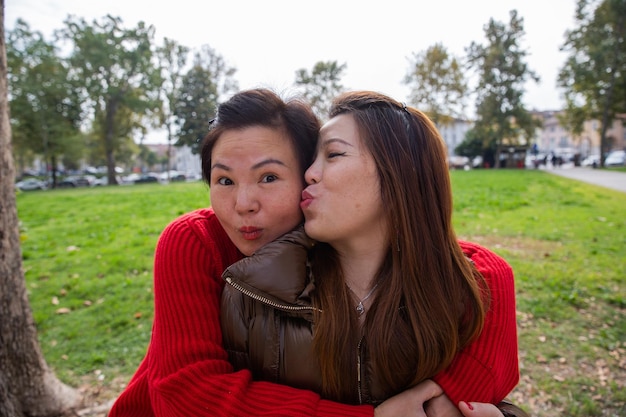 Zwei chinesische Freundinnen umarmen sich im Park. Eine küsst die andere auf die Wange
