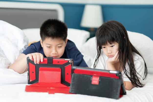 Zwei chinesische Kinder sind Tablet-süchtig asiatisches Kind, das zusammen auf ihrem Bett telefoniert, Kind mit Smartphone