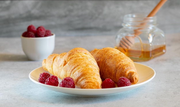 Zwei Croissants mit Himbeeren und Honig auf hellem Betonhintergrund in der Nähe