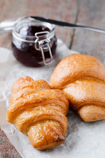 Zwei Croissants und ein Glas Marmelade auf einem Holz