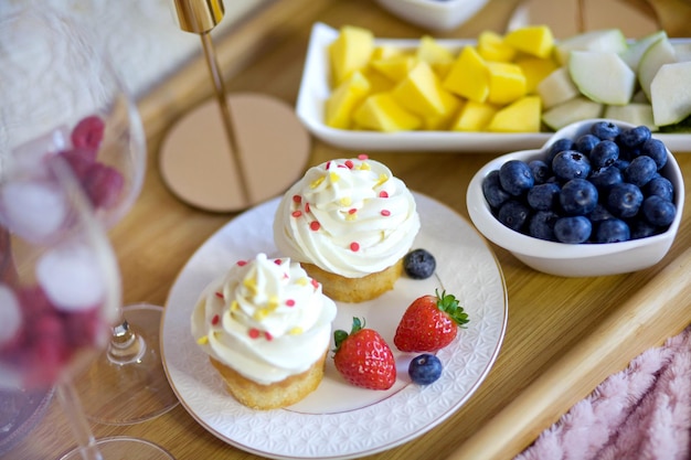 Zwei Cupcakes mit weißen Sahnefrüchten und Beeren auf einem Holztablett