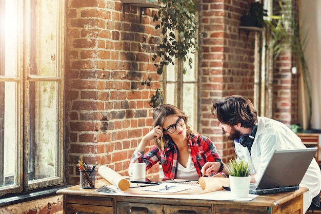 Zwei ehrgeizige Architekten diskutieren über ein Bauprojekt in einem modernen Loft-Büro, das sie mit einem Laptop verwenden