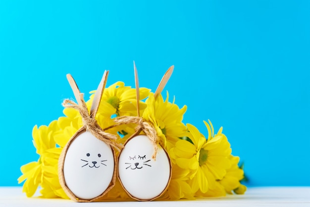 Zwei eier mit zeichnungsgesichtern mit gelben blumen auf einem blauen hintergrund