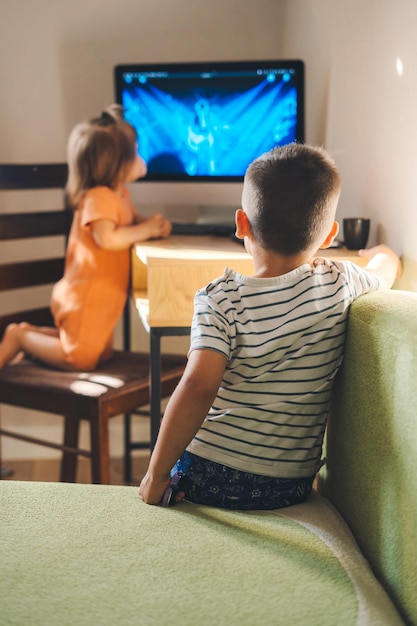 Zwei entzückende kleine Kinder, die fernsehen, wenn sie zu Hause bleiben, wegen Coronavirus Sitzender Lebensstil Sucht nach Gadgets