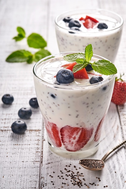 Zwei Erdbeer-Chia-Samen geschichteten Smoothie oder Milchshake mit Erdbeer- und Blaubeerminze im Glas auf hellgrauem Hintergrund. Sommer und gesunde Diätgetränke, vegetarisches Lebensmittelkonzept.