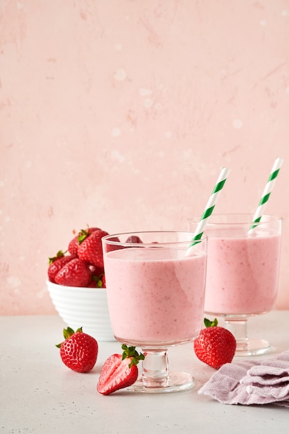 Zwei Erdbeer-Smoothie oder Milchshake mit Beeren und Minze im Glas auf hellrosa Hintergrund. Sommergetränkshake, Milchshake und Erfrischungs-Bio-Konzept. Gesunde Ernährung, vegetarisches Lebensmittelkonzept.