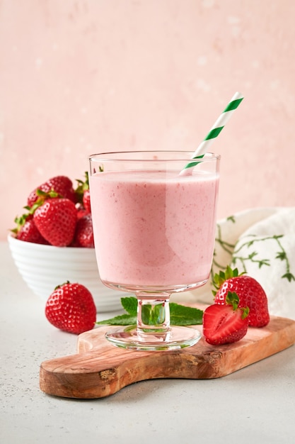 Zwei erdbeer-smoothie oder milchshake mit beeren und minze im glas auf hellrosa hintergrund. sommergetränkshake, milchshake und erfrischungs-bio-konzept. gesunde ernährung, vegetarisches lebensmittelkonzept.