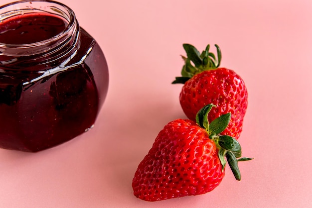 Zwei Erdbeeren und Erdbeermarmelade auf rosa Hintergrund