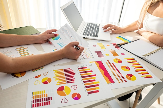 Zwei erfolgreiche, stylische junge Mädchen sitzen im Büro am Tisch und beobachten Verkaufscharts Graphs-Konzept