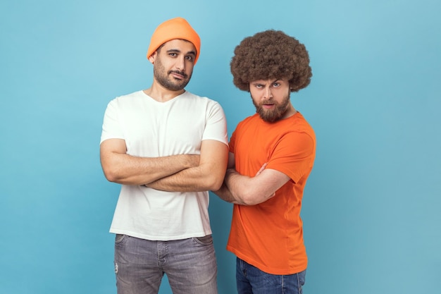 Foto zwei ernsthafte hipster-männer, die mit durchsetzungsfähigem ausdruck in die kamera blicken und die hände gefaltet halten