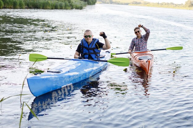 Foto zwei erwachsene männer sitzen in einem kajak und grüßen das konzept der wasseraktivitäten