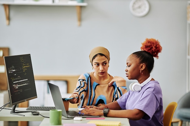 Zwei ethnische junge Frauen, die Computer verwenden und an der Softwareentwicklung arbeiten