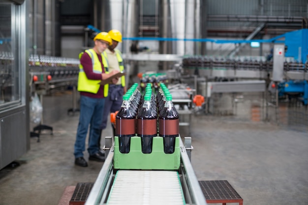 Zwei Fabrikarbeiter überwachen kalte Getränkeflaschen in der Produktionslinie