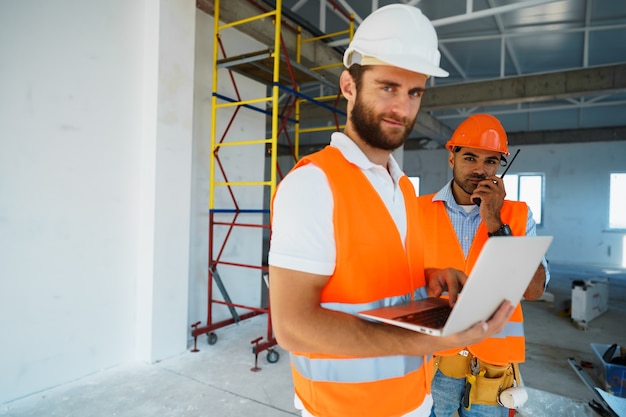 Zwei Fachaufseher in Bauarbeiterhelmen mit Laptop auf der Baustelle für die Arbeit