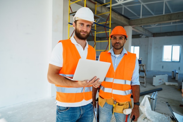 Zwei Fachaufseher in Bauarbeiterhelmen mit Laptop auf der Baustelle für die Arbeit