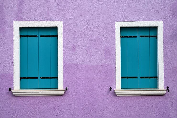 Zwei Fenster mit hellblauen Fensterläden an der alten lila Wand. Italien, Venedig, Burano Insel.