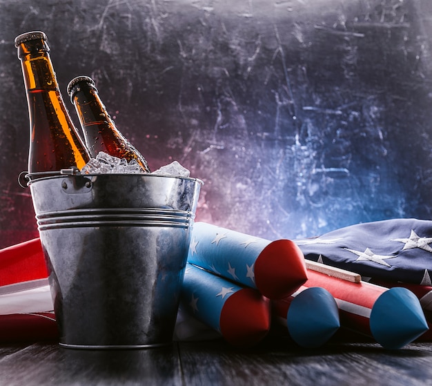 zwei Flaschen Bier in einem Eiskübel mit der amerikanischen Flagge in der Nähe und Raketen für Feuerwerk. Feierkonzept zum Unabhängigkeitstag