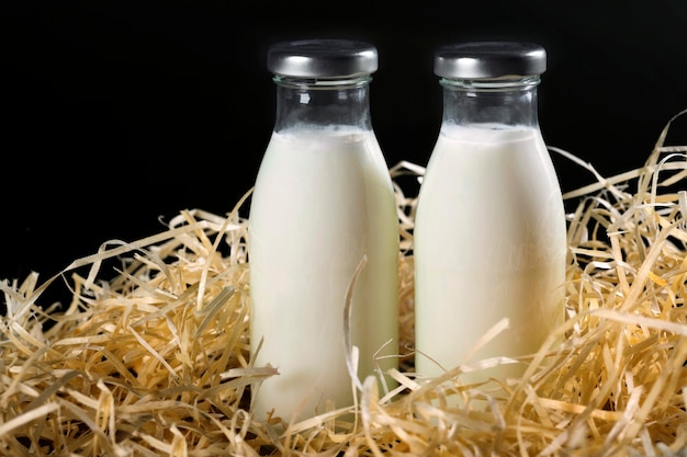 Foto zwei flaschen frische milch im heu auf schwarzem hintergrund gesunde ernährung