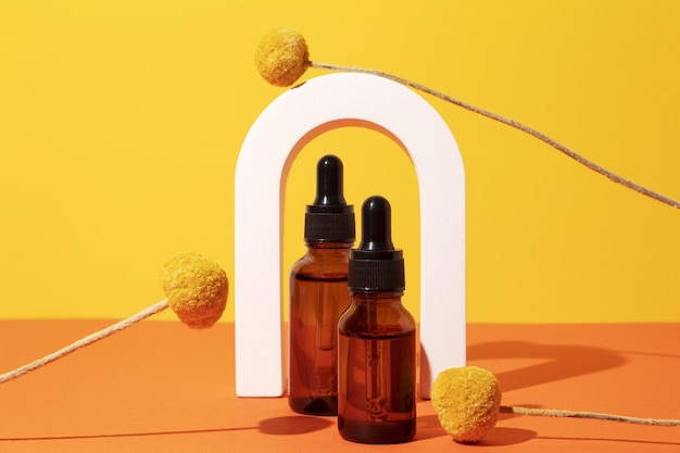 Zwei Flaschen unterschiedlicher Größe mit Serum im Bogen mit Blütenextrakten Craspedia-Blüten Hautpflegekosmetik Hyaluronsäure-Ölserum mit Kollagen und Peptiden