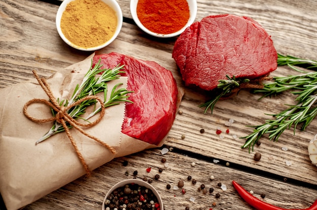 zwei Fleischstücke aus der Metzgerei, ein Stück Fleisch in Papier eingewickelt. Ein Stück Rindfleisch in Form eines Steaks auf Holz mit Zutaten