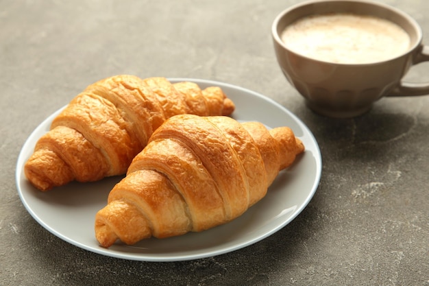 Zwei französische Croissants auf Teller und Tasse Kaffee auf konkretem Hintergrund